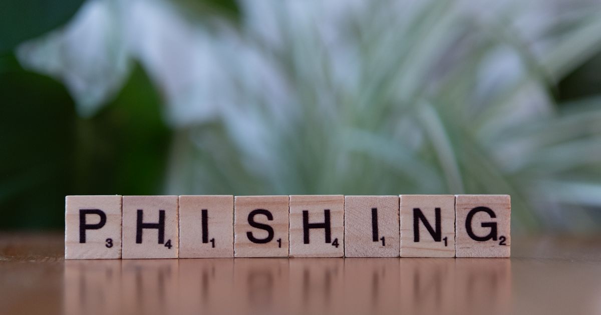 Wooden letter tiles spelling out phishing beside a keyboard, illustrating credential-theft attacks