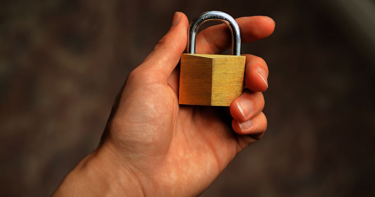 A hand holding a brass padlock, symbolizing account security and smartphone privacy protection