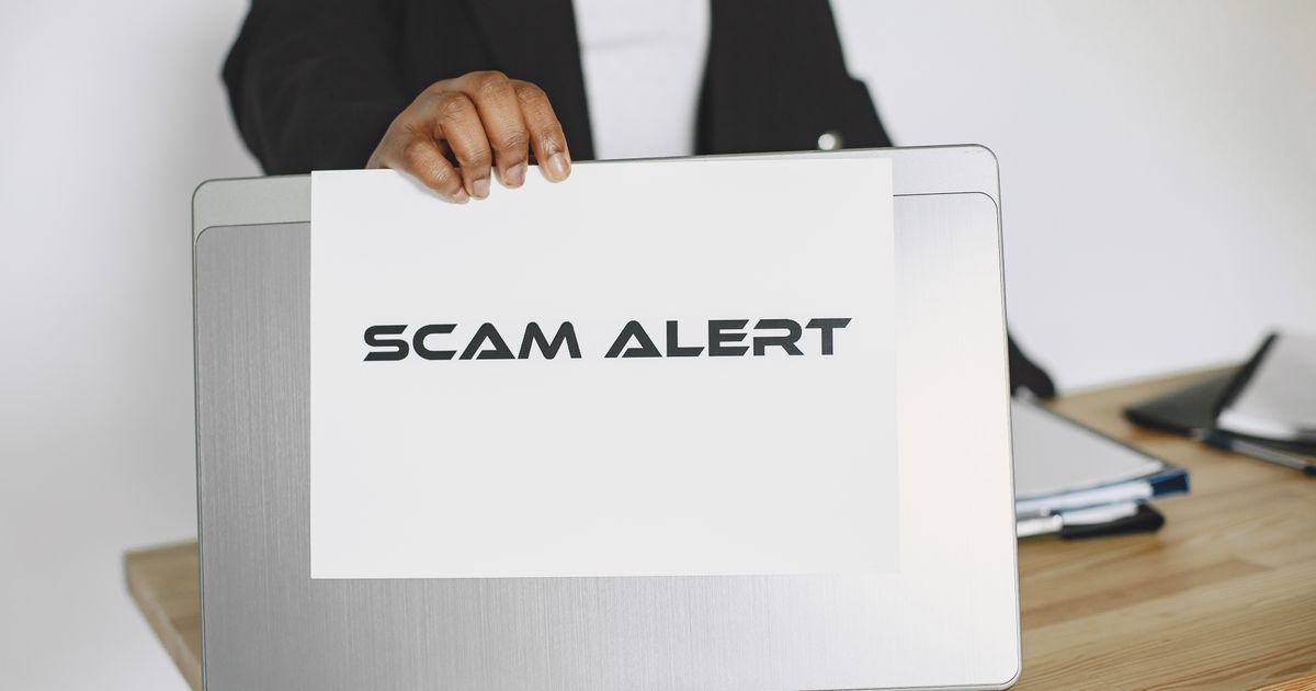 A person holds a scam alert warning sign above a laptop